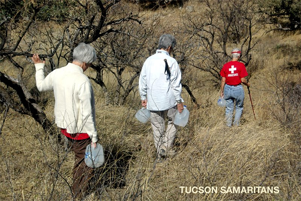 Photo of 3 volunteers carrying water out into the desert